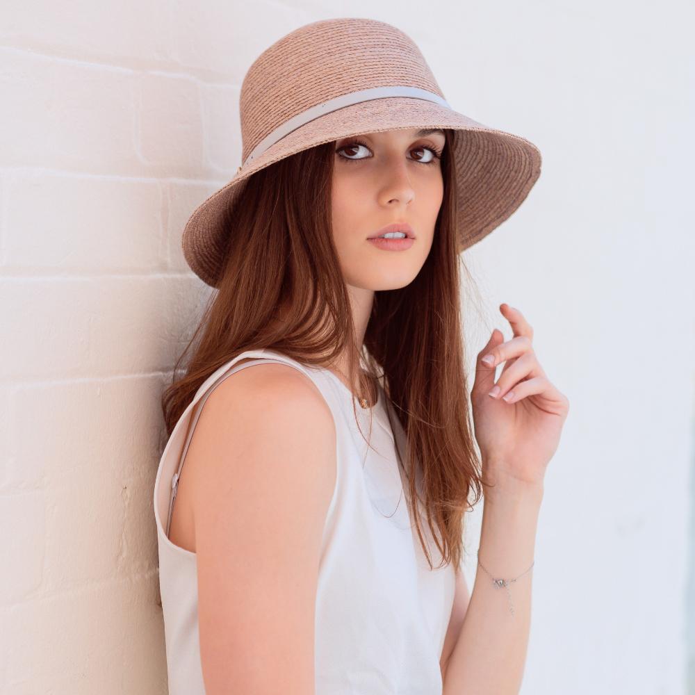 Female Model wearing Straw Hat and White Top standing in front of a white brick wall