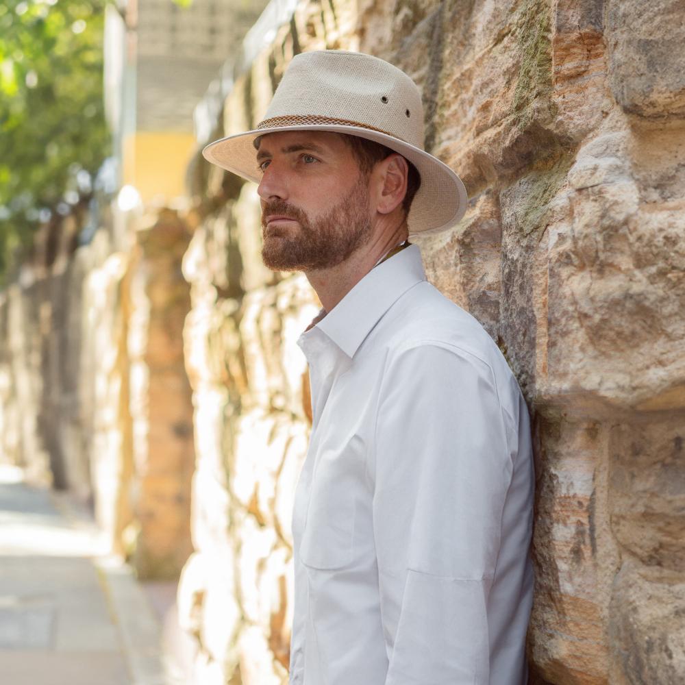 Male model standing in front of white brick wall wearing an outdoor style hat