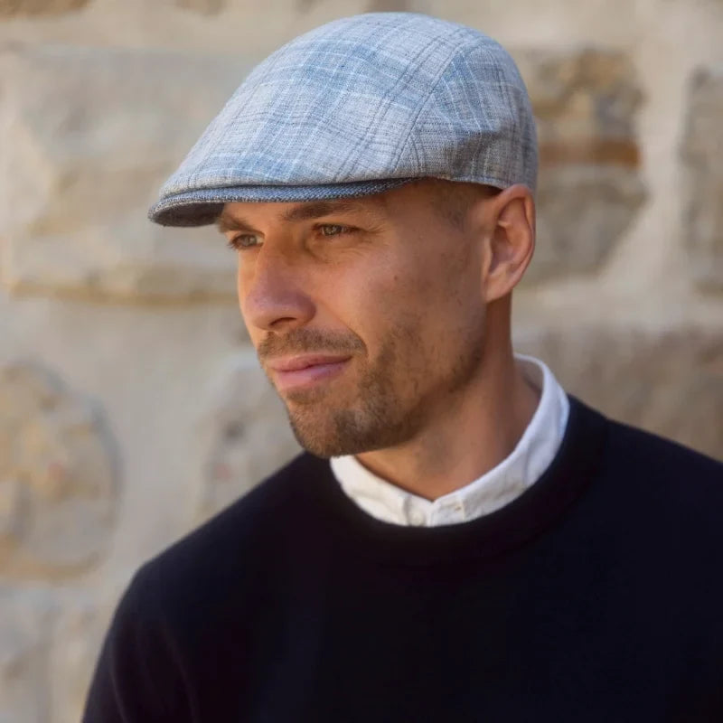 Male Model wearing blue check coloured Flat Cap standing in front of a stone wall
