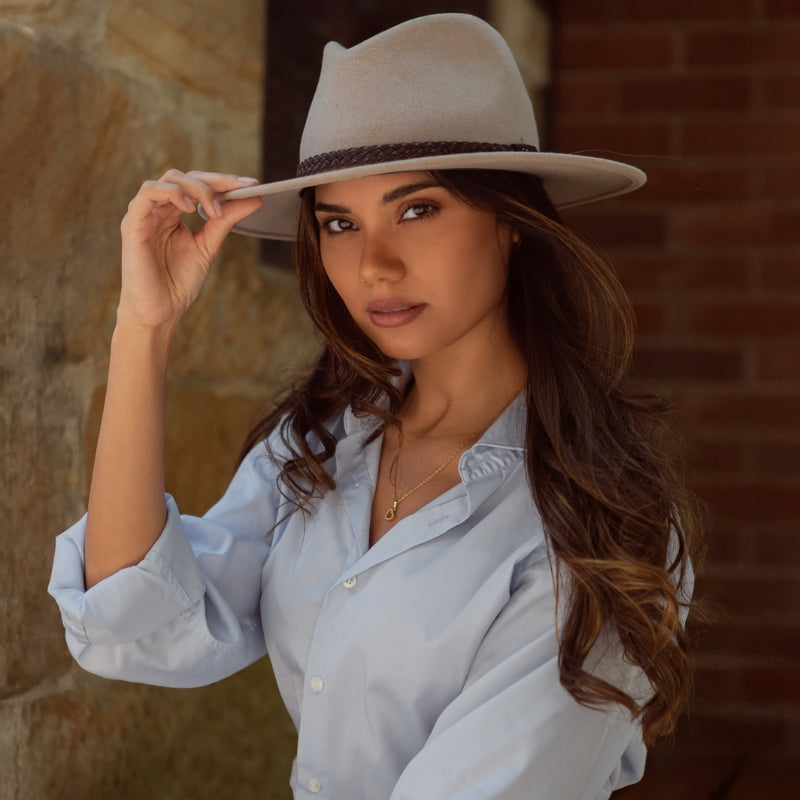 Female Model sitting in front of sandstone wall, wearing a brown felt hat