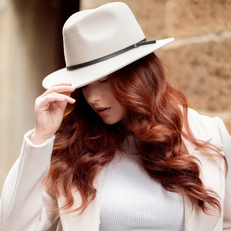 Female Model holding straw hat behind her back in front of a cobblestone street and a sandstone wall
